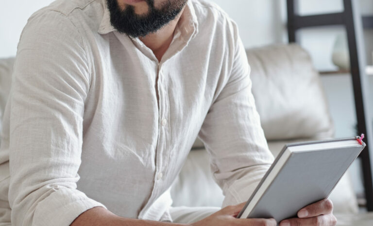 Man sitting on couch, holding gratitude journal and looking away